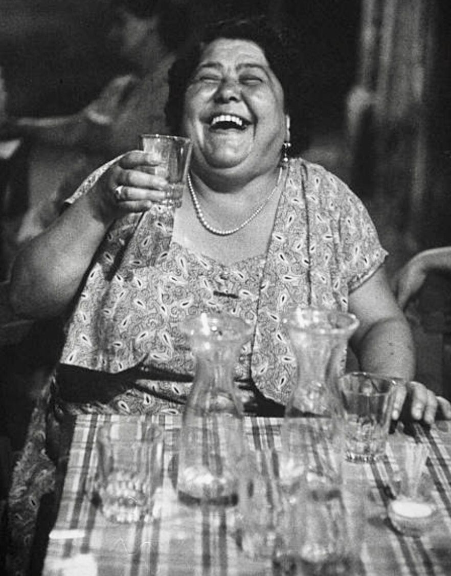 A woman laughing with a glass raised at a table set with wine carafes, an old family photograph